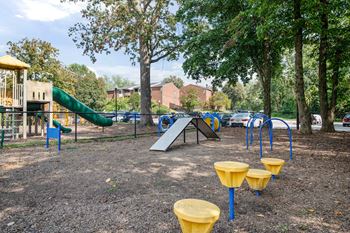 A playground with a green slide, a yellow and blue play structure, and yellow and blue swings.